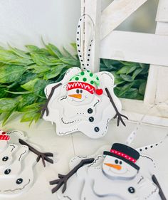 two snowmen with hats and scarfs are hanging from a white chair next to green leaves