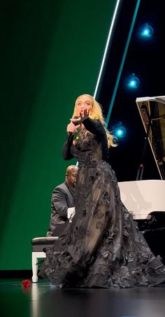 lady in black dress sitting on piano with man standing behind her and lighting up the stage