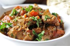 a white bowl filled with meat and vegetables on top of a table next to bread