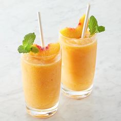 two glasses filled with orange juice and garnished with mint leaves, on a marble surface