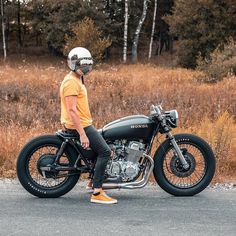 a man in an orange shirt and helmet sitting on a black motorbike by the road