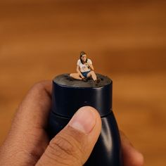 a tiny figurine is sitting on top of a black bottle with a man in it