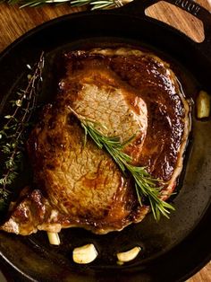 a steak in a skillet with herbs on the side