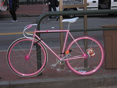 a pink bike parked on the side of a street next to a fence and sidewalk