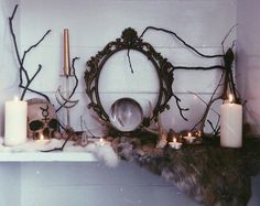 candles are lit on a mantle with branches around it and an ornate mirror in the middle