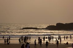 many people are standing on the beach at sunset