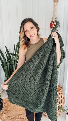 a woman holding up a green knitted blanket