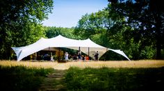 a group of people standing under a white tent in the middle of a grass covered field