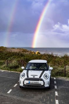 a white car parked in front of a rainbow on the ocean with a sky background