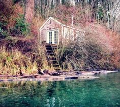 a small cabin sitting on top of a hill next to water