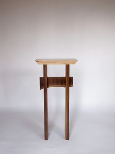 a small wooden table sitting on top of a white floor next to a gray wall