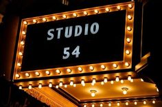 a sign that says studio 54 lit up at night with lights around it and the number 54