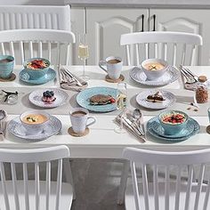 a white table topped with plates and cups filled with food next to two white chairs