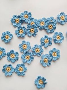 crocheted blue and yellow flowers are scattered on a white surface, with one flower in the center