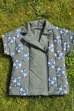 a jacket laying on the grass with flowers and blue trimmings, in front of it