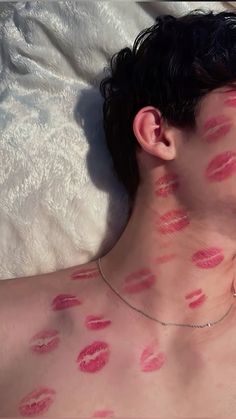 a man laying on top of a bed covered in lots of red lipstick kisses all over his body