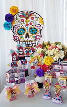 a table topped with lots of candy and flowers next to a sugar skull wall hanging on the wall