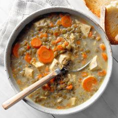 a bowl of soup with carrots and meat in it next to a piece of bread