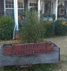 a merry christmas sign sitting on top of a wooden bench in front of a house