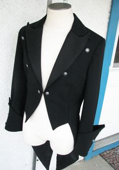 A classic dress coat with gothic detailing. This piece has peak lapels and a curved upper collar so that the points overlap. The fronts of the tailcoat just kiss and finish with a hook and eye. The unique pointed cuffs feature 6 buttons. And the back tightens with a belt. The piece is made from a gorgeous 12oz wool suiting. ----------------------------------- We can make a tailcoat in any style. From steampunk, to Regency, to stunning white tie. Contact us with the details that you would like be Steampunk Long Sleeve Formal Outerwear, Gothic Formal Winter Outerwear, Victorian Black Formal Outerwear, Gothic Black Outerwear For Formal Occasions, Black Gothic Outerwear For Formal Occasions, Elegant Black Blazer For Costume, Fitted Double-breasted Tuxedo For Winter, Fitted Double-breasted Winter Tuxedo, Victorian Style Formal Long Coat