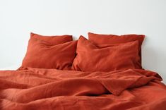 a bed with red sheets and pillows on top of it, against a white wall