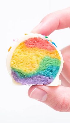 a hand holding a rainbow cake with white frosting