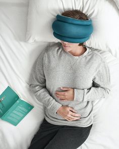 a woman laying in bed with her stomach covered by a head pillow and book next to it