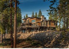 a large wooden house sitting on top of a hill surrounded by pine trees and rocks