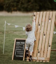 a little boy playing on a wooden structure in the grass next to a chalkboard sign