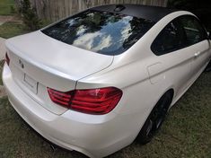 the rear end of a white bmw car parked in front of a wooden fence and tree