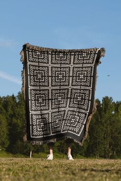 a black and white blanket hanging from the side of a tree covered field with trees in the background