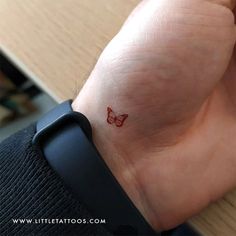 a small red butterfly tattoo on the wrist