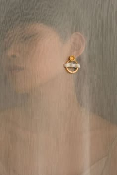 a woman's face behind a sheer curtain with a gold earring on it