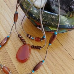 Earth Elements. Smoldering Carnelian. The central stone is dark orange, deeply spiced almost. Multi-strand, three, includes blue turquoise beads. Lots of seasonal contrast with tinted wood. The mood is sultry, with fiery effects. Good layering statement. Threaded on a natural brown cord. 20" length. Lobster clasp. Gift boxed. VINTAGE Artisan Orange Beads, Gems, And Cabochons For Gifts, Bohemian Orange Beaded Necklaces With Gemstones, Orange Gemstone Bohemian Beaded Necklace, Orange Bohemian Beaded Necklace With Gemstones, Bohemian Orange Beaded Necklace With Gemstones, Bohemian Gemstone Beads And Cabochons In Brown, Bohemian Brown Gemstone Beads And Cabochons, Bohemian Brown Beads Gems And Cabochons For Gifts, Bohemian Brown Beads And Cabochons For Gifts