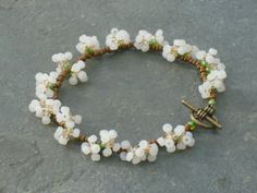 a bracelet with white flowers and green beads on a stone surface next to a pair of scissors