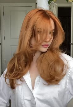 a woman with long red hair standing in front of a mirror wearing a white shirt