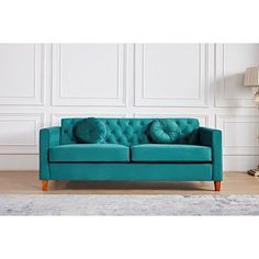 a teal colored couch in front of a white wall with a lamp on it