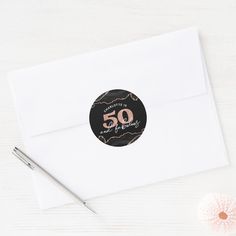 a white envelope with a black and pink 50th birthday sticker on it next to a pen