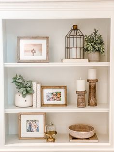 a white book shelf with pictures and other items on it, including candles, vases, plants and photos