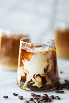 two glasses filled with iced coffee on top of a white table covered in coffee beans