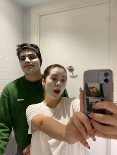 two people with face paint taking a selfie in front of a mirror while holding a cell phone