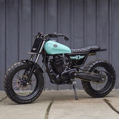 a blue and black motorcycle parked in front of a gray metal wall on the sidewalk