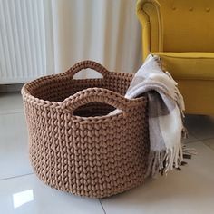 a brown basket sitting on top of a white floor next to a yellow chair and blanket