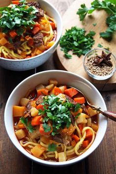 two bowls of soup with meat, carrots and parsley on a wooden table