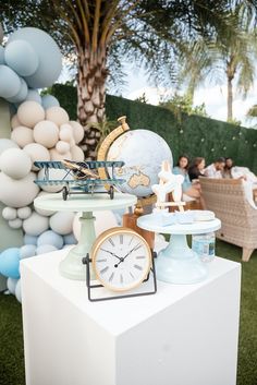 a table topped with a clock next to balloons and other decorations on top of a grass covered field