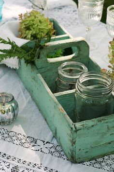 an old wooden box filled with mason jars and greenery on a tablecloth covered table