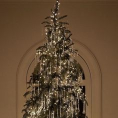 a white christmas tree with lights hanging from it's branches in front of a doorway