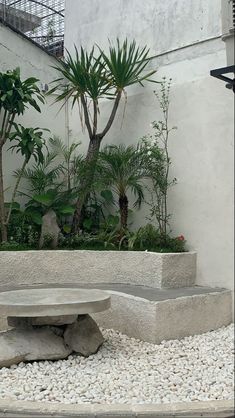 a concrete bench sitting in the middle of a garden filled with plants and rocks next to a building