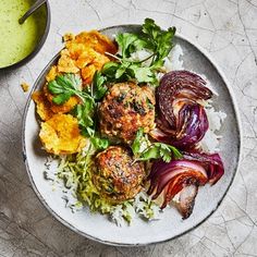 a white plate topped with meatballs and vegetables next to a bowl of green sauce