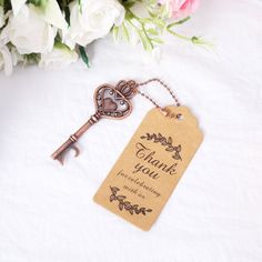 a key with a thank you tag attached to it sitting on a table next to flowers